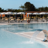 Piscina con cascata d'acqua e lettini sotto ombrelloni bianchi.