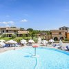 Piscina con ombrelloni bianchi, lettini e edifici in pietra sullo sfondo.