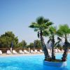 Piscina con palme al centro, circondata da sdraio bianche.