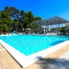 Piscina azzurra circondata da sdraio, con alberi e cielo sereno sullo sfondo.