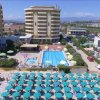 Piscina con ombrelloni verdi e un grande edificio sullo sfondo.