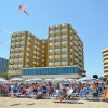 Spiaggia affollata con ombrelloni bianchi e palazzi sullo sfondo.