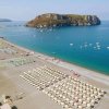 Una spiaggia con ombrelloni beige e un'isola rocciosa in lontananza.