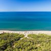 Spiaggia con sabbia dorata e mare blu, circondata da vegetazione verde.