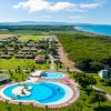 Vista aerea di un resort con piscine circolari, giardini e mare sullo sfondo.