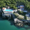 Complesso su una scogliera con piscina, circondato da vegetazione e vista sul mare.